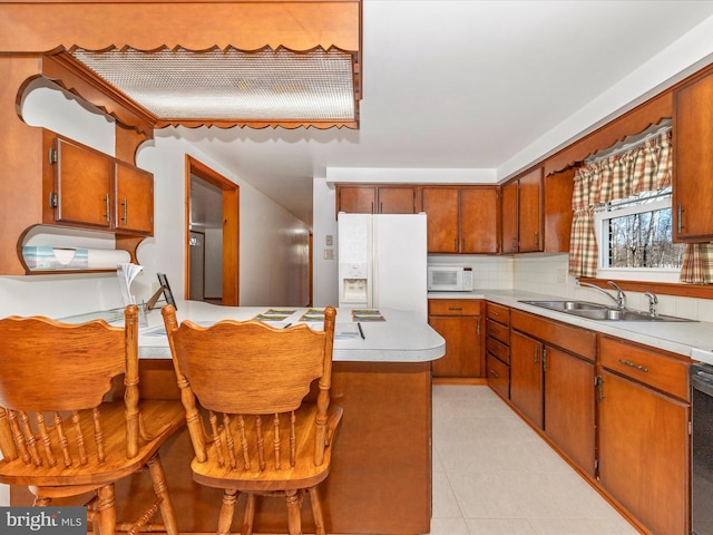 kitchen with sink, white appliances, light tile patterned floors, backsplash, and a kitchen breakfast bar