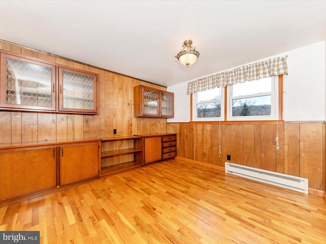 empty room with light wood-type flooring, baseboard heating, and wood walls