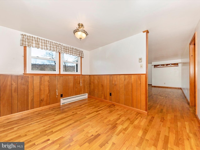 spare room with light hardwood / wood-style flooring, a baseboard radiator, and wood walls