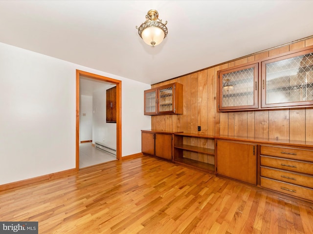 unfurnished room featuring baseboard heating, light hardwood / wood-style flooring, and wood walls