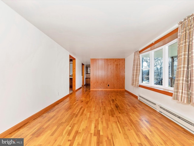 empty room with a baseboard heating unit, light hardwood / wood-style floors, and wood walls