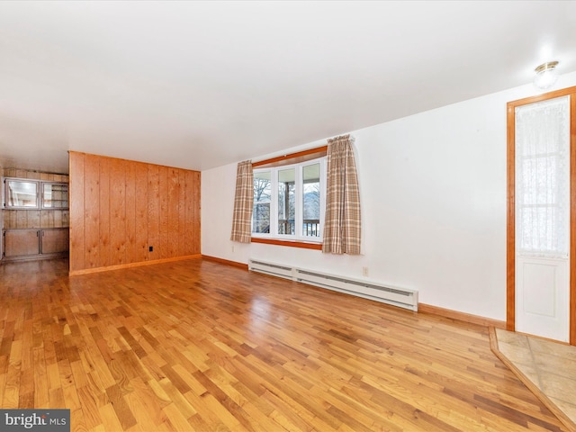 unfurnished living room featuring baseboard heating, light hardwood / wood-style floors, and wood walls