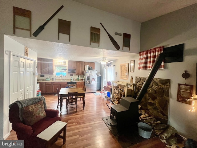 living room featuring a high ceiling, ceiling fan, a wood stove, and light hardwood / wood-style floors