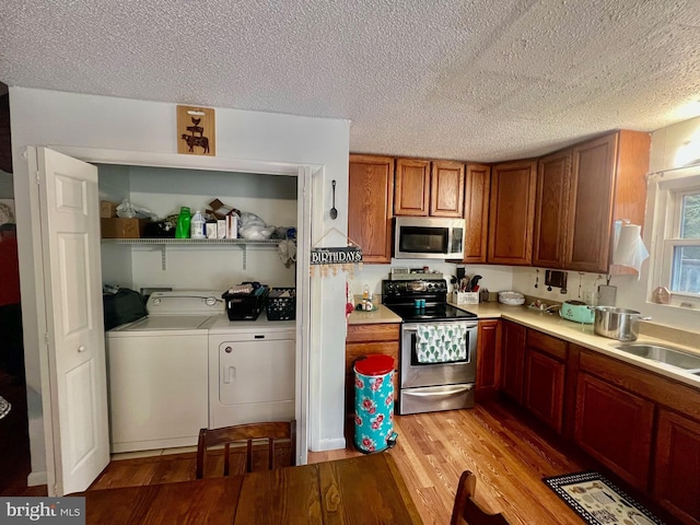 kitchen featuring sink, washing machine and dryer, a textured ceiling, stainless steel appliances, and light hardwood / wood-style floors