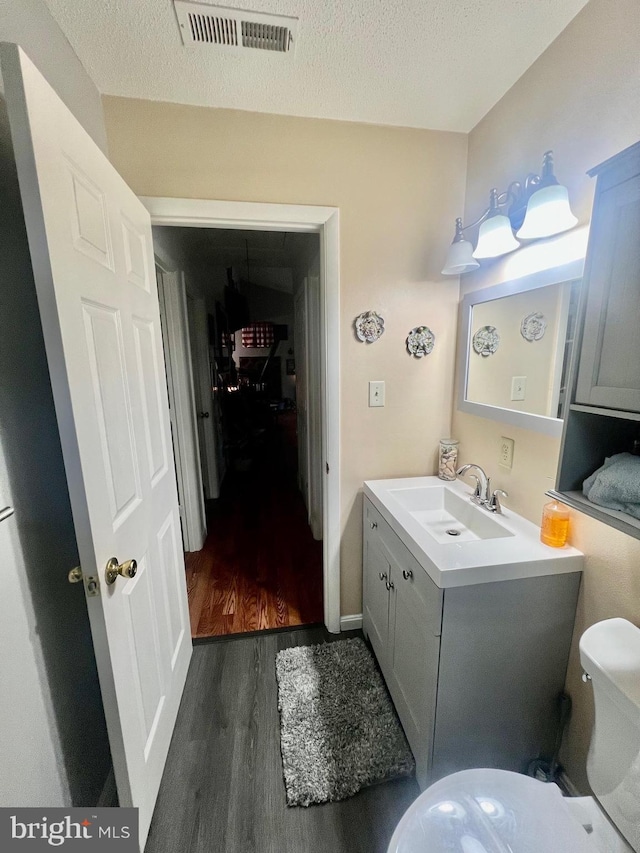 bathroom featuring vanity, wood-type flooring, toilet, and a textured ceiling