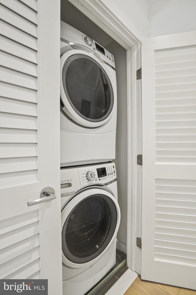 clothes washing area featuring laundry area, wood finished floors, and stacked washer / drying machine