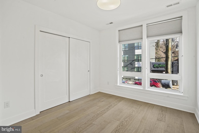 unfurnished bedroom with light wood-style flooring, a closet, visible vents, and baseboards