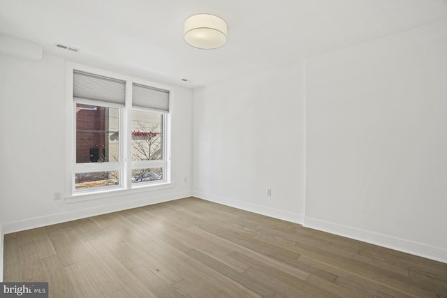 unfurnished room featuring wood finished floors, visible vents, and baseboards