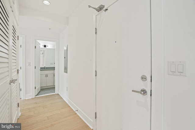 corridor with light wood-type flooring, electric panel, baseboards, and recessed lighting