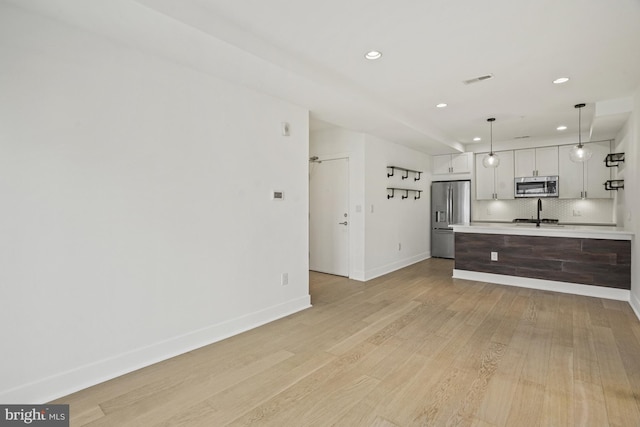 kitchen with stainless steel appliances, light countertops, decorative backsplash, light wood-style floors, and baseboards