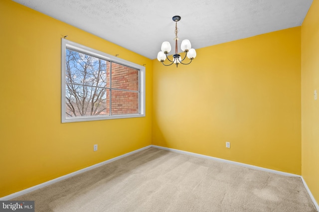 carpeted empty room featuring a notable chandelier and a textured ceiling