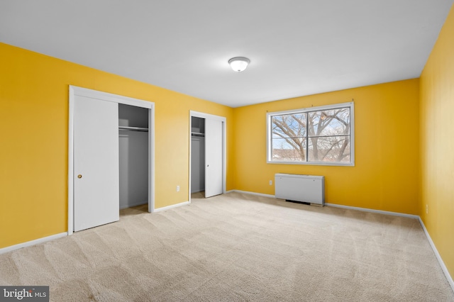 unfurnished bedroom with radiator, two closets, and light colored carpet