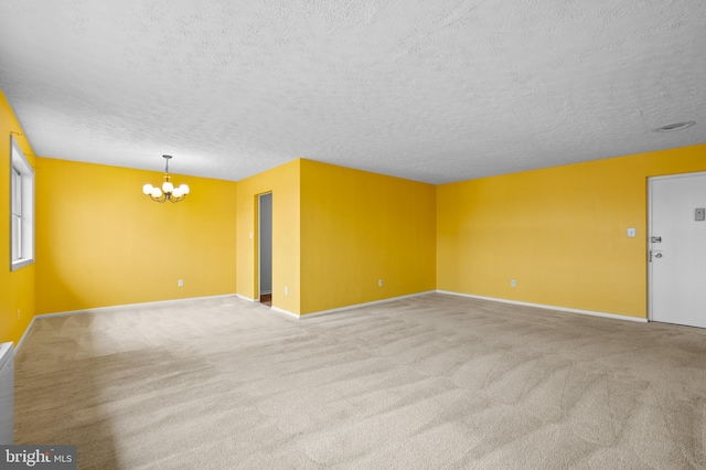 carpeted spare room featuring a notable chandelier and a textured ceiling