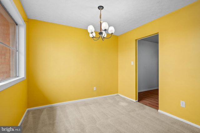 empty room featuring light colored carpet, a textured ceiling, and a chandelier