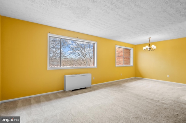 empty room with a textured ceiling, light colored carpet, and a chandelier