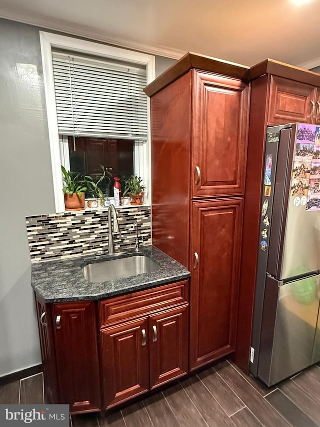 kitchen with dark stone countertops, stainless steel fridge, sink, and backsplash