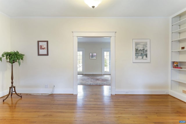 unfurnished room featuring built in shelves, ornamental molding, and wood-type flooring