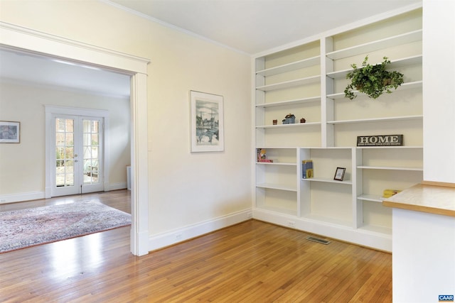 unfurnished room featuring hardwood / wood-style floors, built in features, ornamental molding, and french doors