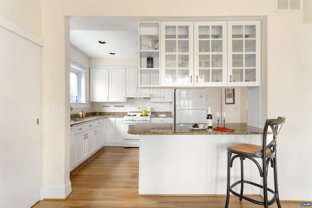 kitchen with white appliances, white cabinetry, light hardwood / wood-style floors, kitchen peninsula, and dark stone counters