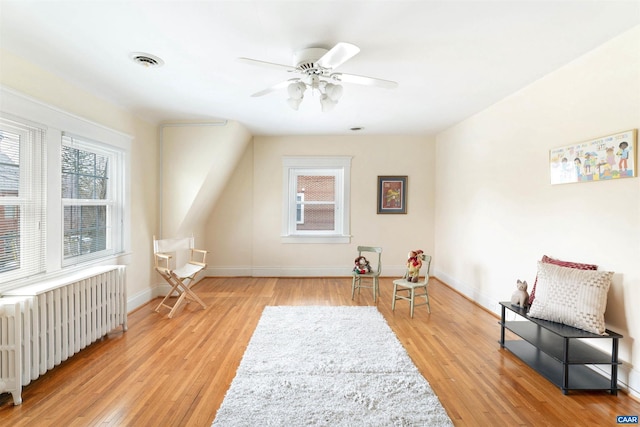 living area with radiator heating unit, ceiling fan, and light wood-type flooring