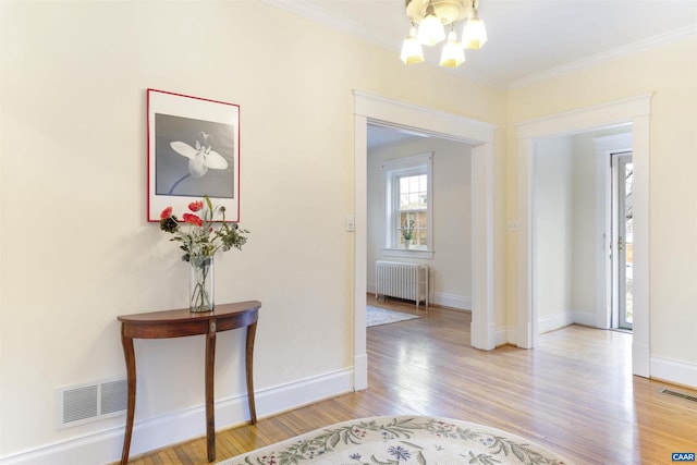 interior space featuring an inviting chandelier, radiator, light hardwood / wood-style flooring, and ornamental molding