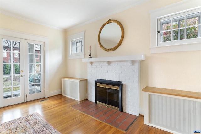 unfurnished living room featuring crown molding, a fireplace, french doors, and hardwood / wood-style flooring