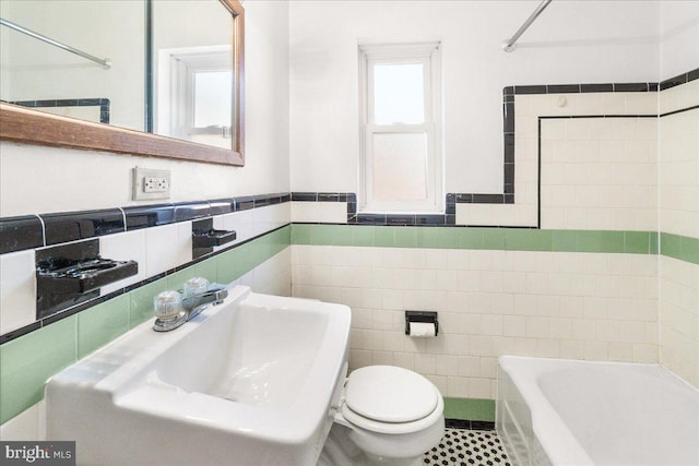 bathroom with tile patterned floors, a tub to relax in, toilet, sink, and tile walls