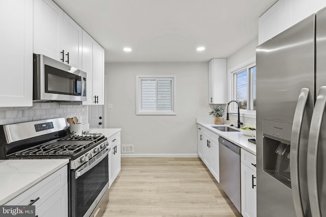 kitchen with appliances with stainless steel finishes, white cabinetry, sink, backsplash, and light stone counters