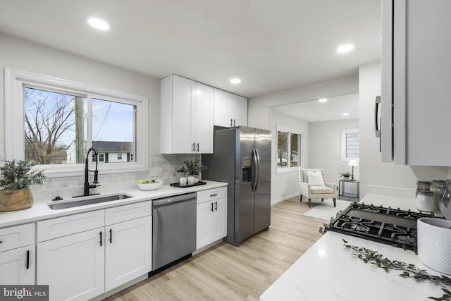 kitchen with appliances with stainless steel finishes, sink, white cabinets, decorative backsplash, and light wood-type flooring