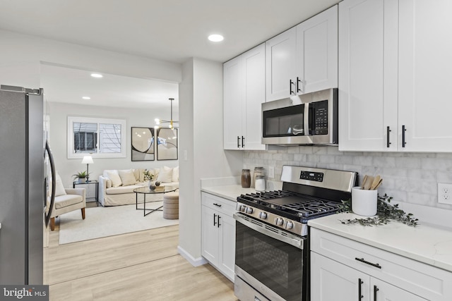 kitchen featuring appliances with stainless steel finishes, tasteful backsplash, white cabinets, light stone countertops, and light hardwood / wood-style flooring