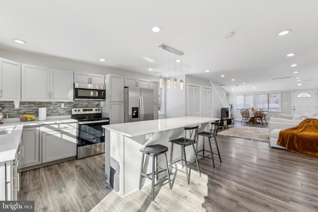 kitchen with a kitchen bar, hanging light fixtures, light wood-type flooring, a kitchen island, and stainless steel appliances