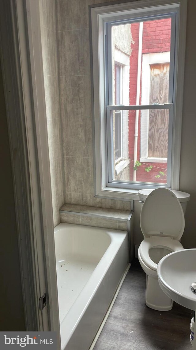 bathroom with hardwood / wood-style flooring, a tub to relax in, and toilet