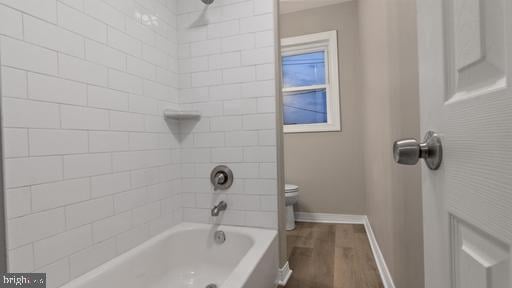 bathroom with hardwood / wood-style floors, tiled shower / bath combo, and toilet