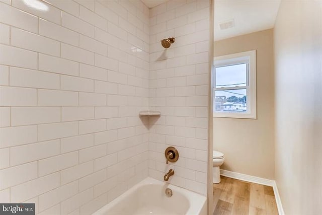 bathroom with wood-type flooring, toilet, and tiled shower / bath