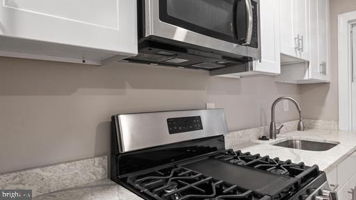 kitchen featuring light stone counters, appliances with stainless steel finishes, sink, and white cabinets