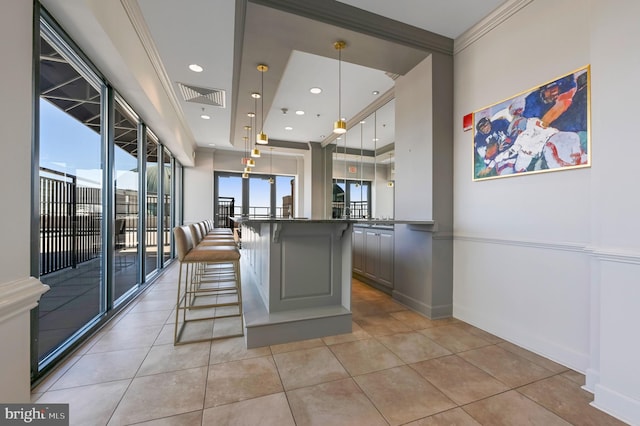 kitchen with light tile patterned floors, a breakfast bar, gray cabinetry, ornamental molding, and decorative light fixtures