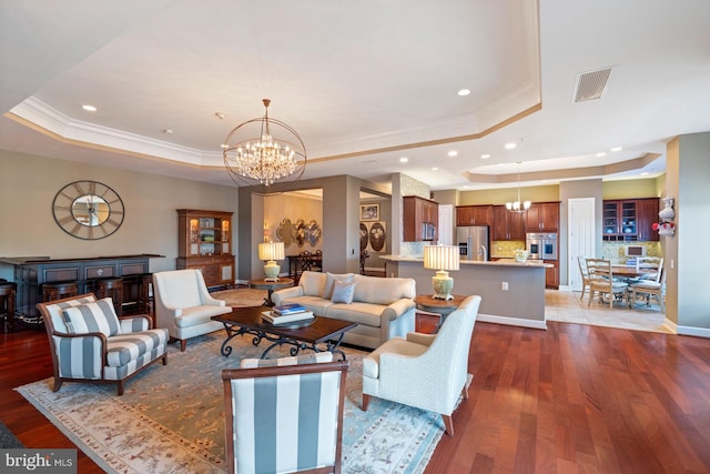 living room with a raised ceiling, crown molding, dark hardwood / wood-style floors, and an inviting chandelier