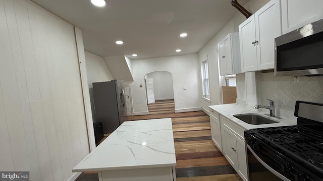 kitchen featuring sink, a center island, stainless steel appliances, light stone countertops, and white cabinets