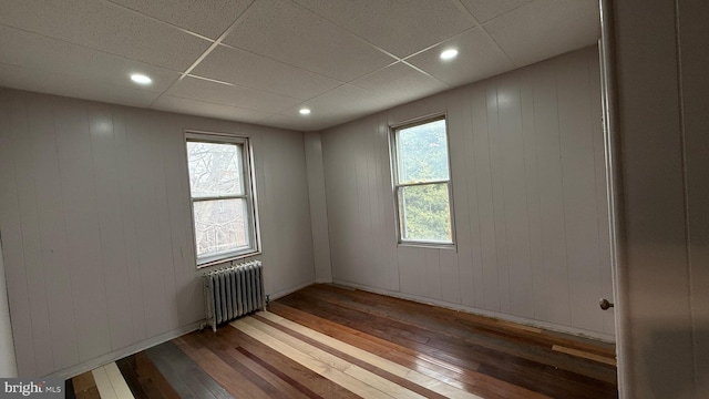 empty room featuring a drop ceiling, radiator, and hardwood / wood-style floors