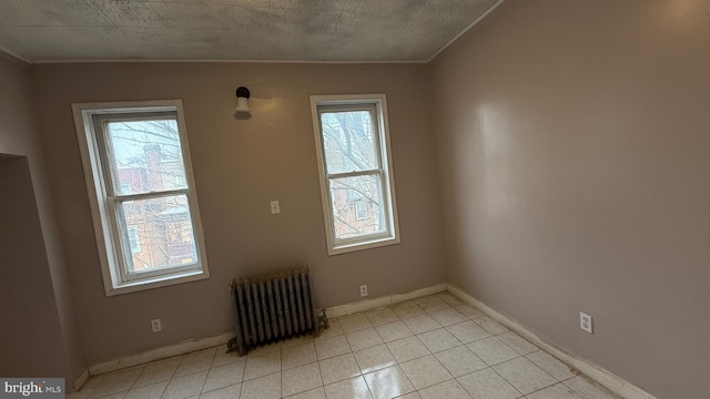 spare room with light tile patterned flooring, crown molding, radiator heating unit, and a textured ceiling