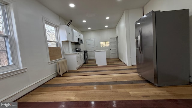 kitchen featuring light hardwood / wood-style flooring, appliances with stainless steel finishes, radiator heating unit, white cabinets, and a baseboard heating unit