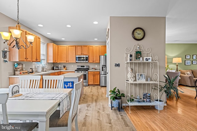 kitchen with light brown cabinetry, light wood-type flooring, appliances with stainless steel finishes, a notable chandelier, and pendant lighting