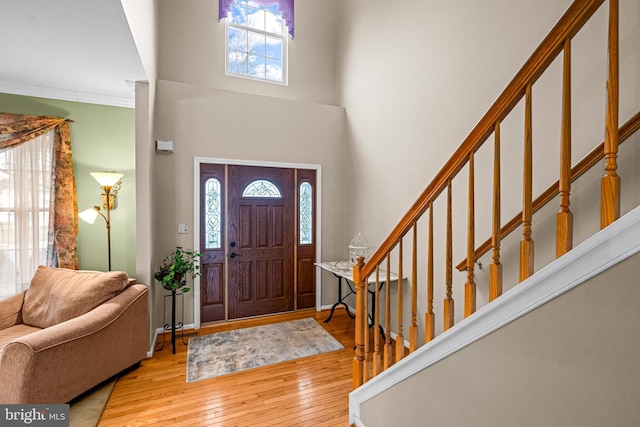 foyer with crown molding, a high ceiling, and light wood-type flooring