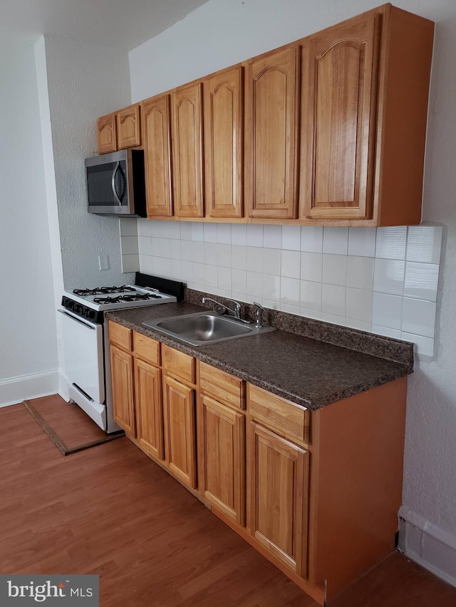 kitchen with hardwood / wood-style flooring, white gas range, sink, and backsplash