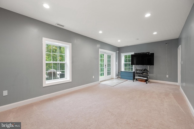 unfurnished living room featuring plenty of natural light, light colored carpet, and french doors