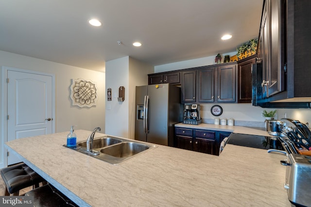 kitchen with dark brown cabinetry, sink, a breakfast bar area, stainless steel fridge, and kitchen peninsula