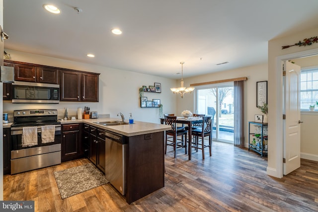 kitchen featuring sink, stainless steel appliances, dark hardwood / wood-style floors, decorative light fixtures, and kitchen peninsula