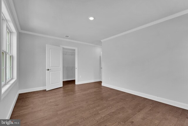 empty room featuring crown molding, dark wood finished floors, and baseboards