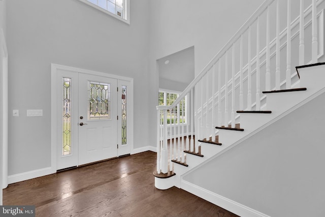 foyer entrance featuring stairs, dark wood finished floors, a towering ceiling, and baseboards