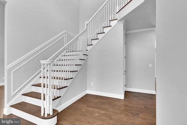 stairs featuring a towering ceiling, crown molding, baseboards, and wood finished floors